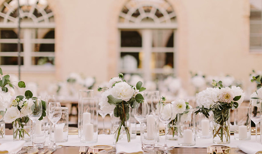 a table set with white flowers and candles with arched windows in background