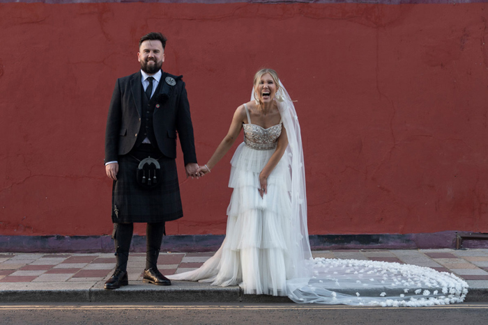 Bride and groom hold hands against red backdrop