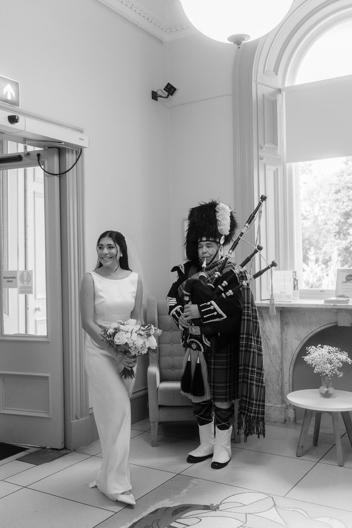 bride stands next to piper on wedding day  at kilmardinny house in bearsden