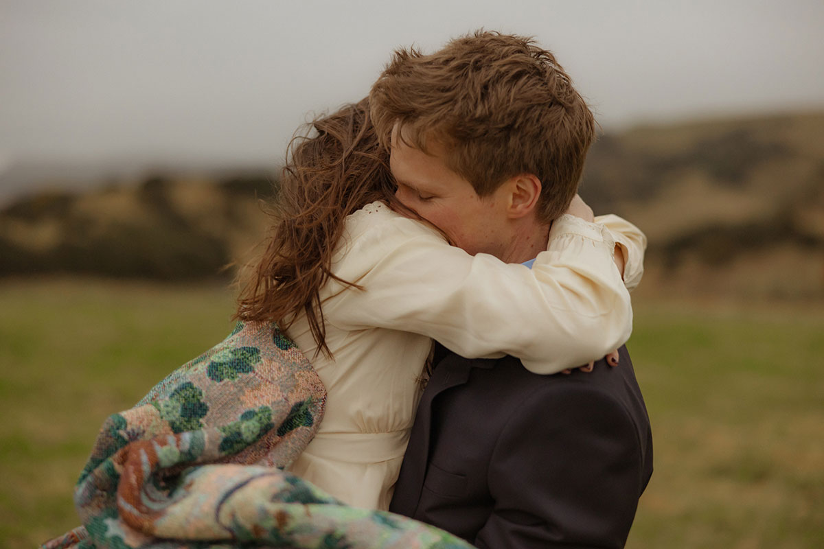 close up picture of bride wearing paisley print scarf hugging groom 