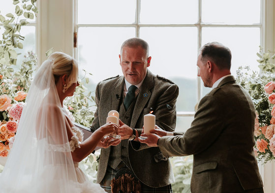 bride, groom and wedding celebrant all hold candles out in front of them for a ceremony ritual 