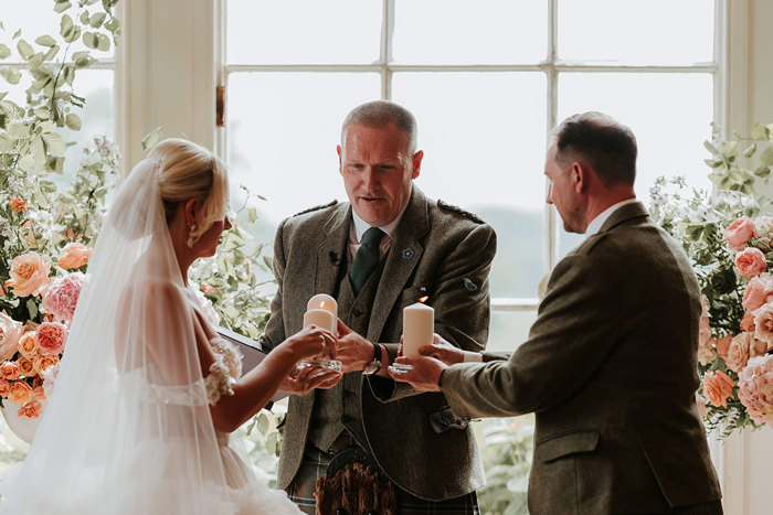 bride, groom and wedding celebrant all hold candles out in front of them for a ceremony ritual 