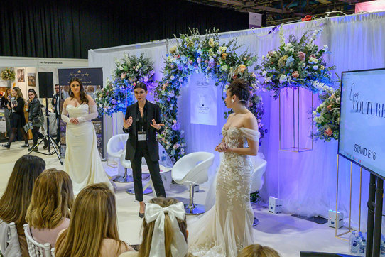 a woman in a black suit giving a presentation to a group of people with a woman in a wedding dress standing on either side of her