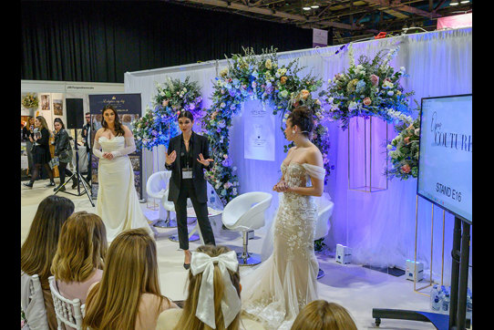 a woman in a black suit giving a presentation to a group of people with a woman in a wedding dress standing on either side of her