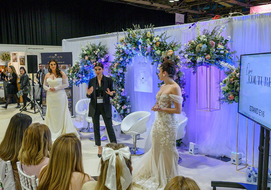 a woman in a black suit giving a presentation to a group of people with a woman in a wedding dress standing on either side of her