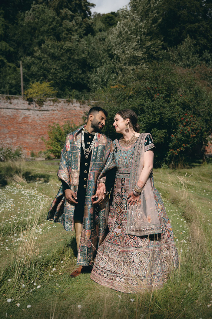 A smiling bride and groom wearing Indian attire walking in the walled garden at Byre of Inchyra.