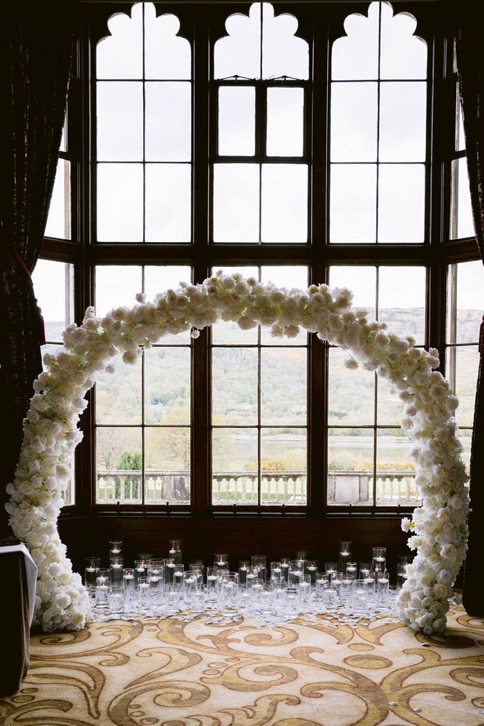 A white flower arch in a room with windows set for a wedding ceremony at Mar Hall.