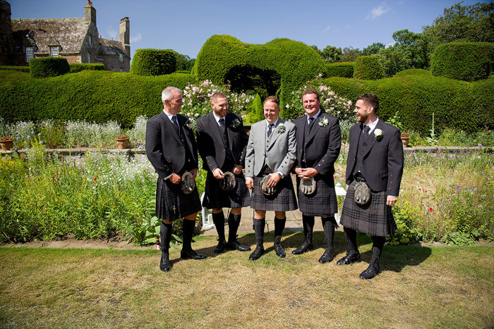 Five men in kilts stand in a sunny garden