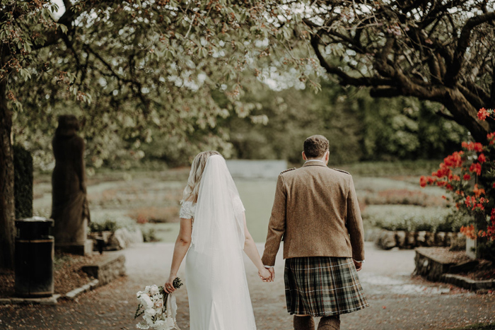 Couple hold hands with back to the camera as they walk in a park