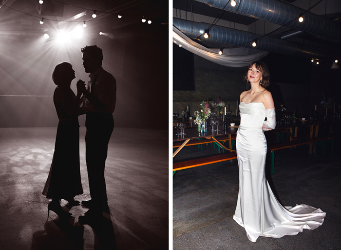 a silhouetted image of people dancing on left. A smiling bride wearing a long white dress with removable sleeves on right. She is standing in front of a long table and bench and there are industrial-looking pipes above her 