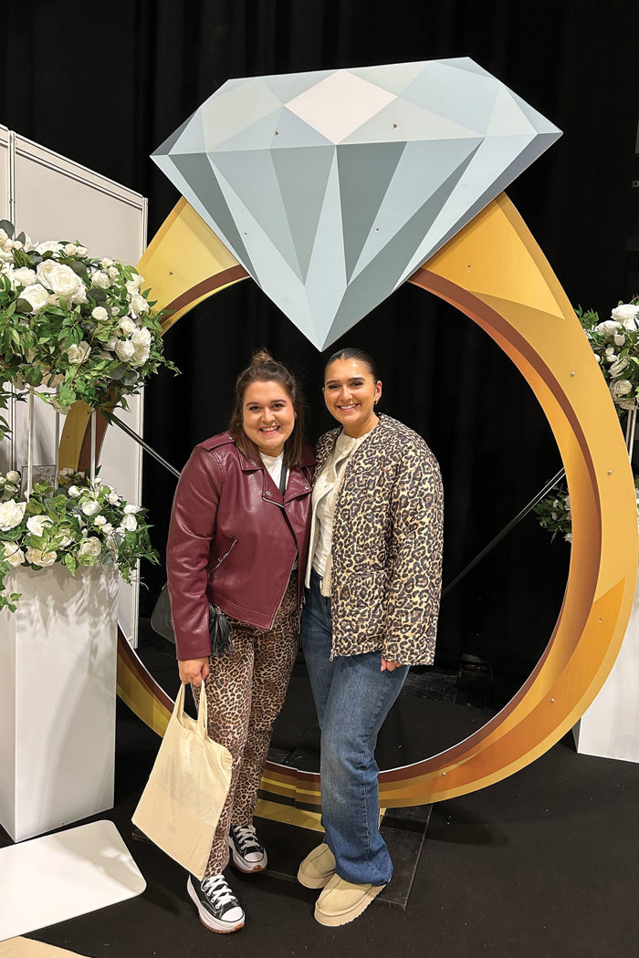 two women posing in front of a large diamond ring cut out