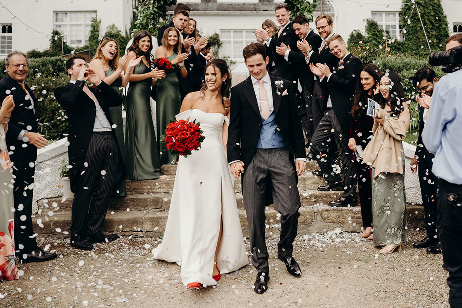 A bride and groom walking down stairs with confetti outside Achnagairn Castle. There are rows of guests either side.