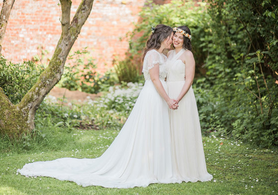 two brides wearing long and fluid wedding dresses standing romantically head-to-head in a walled garden setting at Byre at Inchyra