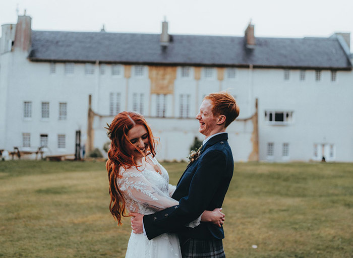 a couple embracing on a lawn outside a building designed by Charles Rennie Mackintosh