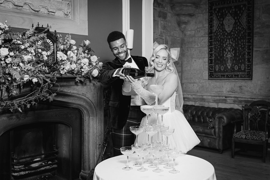 Black and white image of a couple pouring champagne on to champagne tower