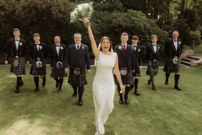 bride cheers while walking in front of groomsmen at kilmardinny house in bearsden