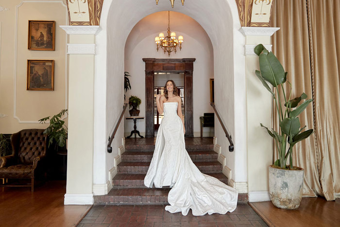 brunette bride in strapless wedding dress with long detachable overskirt smiles and walks down a set of five dark brown brick stairs