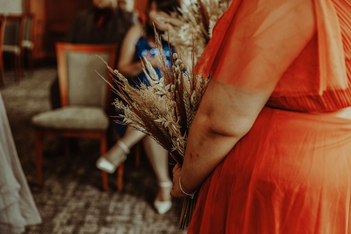 Bridesmaid wearing orange dress holding dried bouquet 