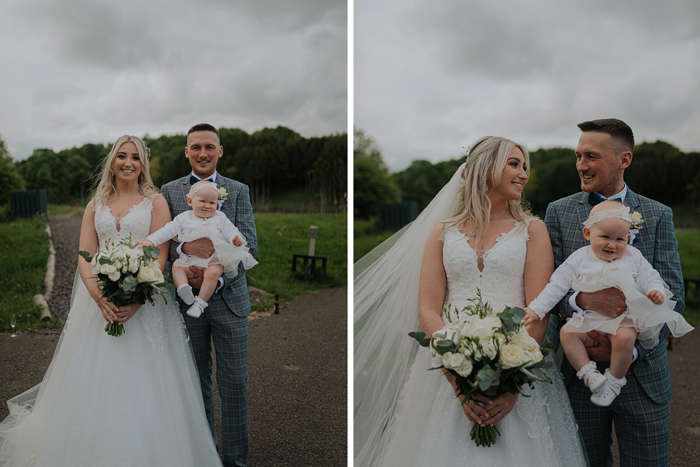 A Newlywed Bride And Groom Pose For Photos, The Groom Holding A Baby With White Flower Ribbon Around Head And The Bride Holding A Large White Bouquet