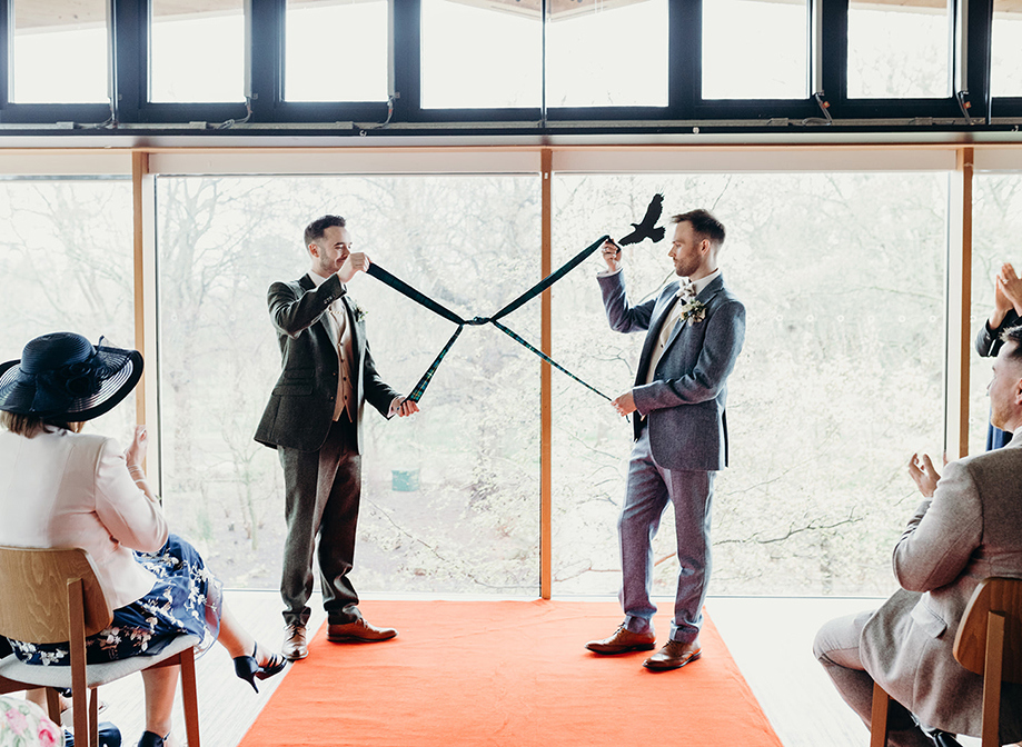 two grooms holding up knotted tartan ribbon after performing a hand fasting at their wedding ceremony