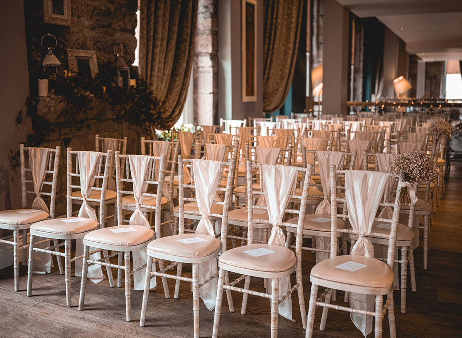 rows of white chiavari chairs with white ribbons tied in the middle of them 