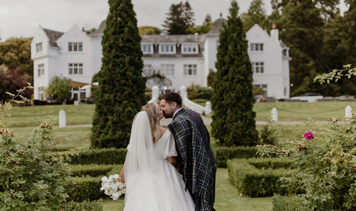 a bride and groom kissing in the garden at Achnagairn Castle