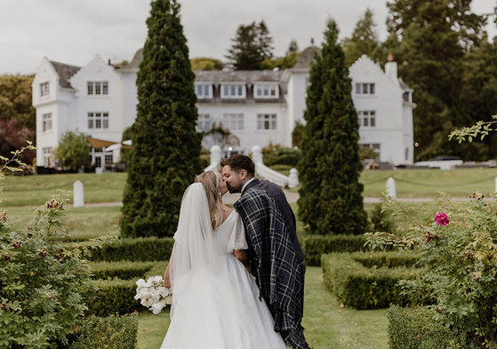 a bride and groom kissing in the garden at Achnagairn Castle