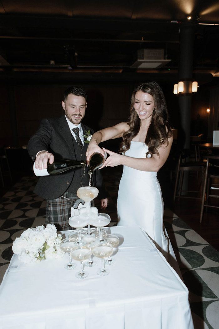 A couple pour bottles of champagne into a champagne tower 