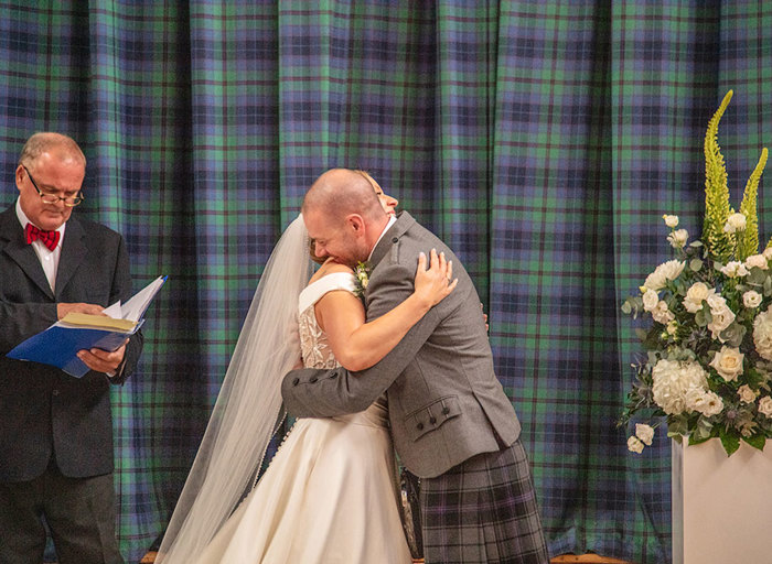 A bride and groom hugging as the officiant stands off to one side