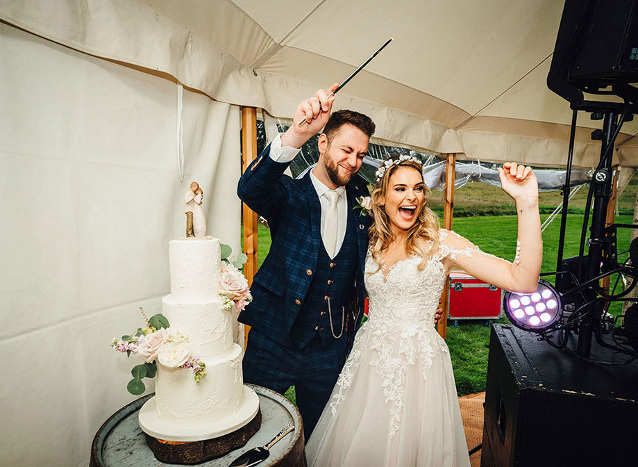 Bride and groom cheer as they get ready to cut into their three-tier wedding cake