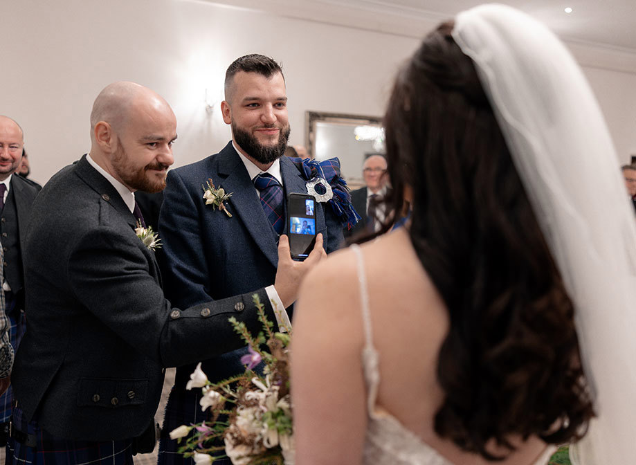 a man showing a bride the screen of a smart phone as groom smiles at her