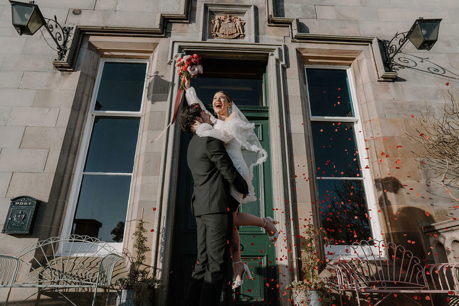 A groom picking up a bride as confetti falls around them