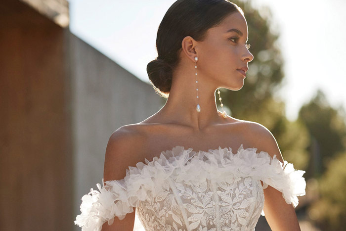 woman in bridal gown that has an off the shoulder neckline with floral applique detailing