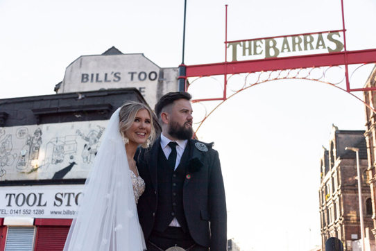 Bride and Groom stand under Barras sign in Glasgow