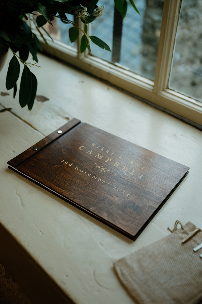 a dark wooden wedding guest book sitting on a wooden ledge by a window