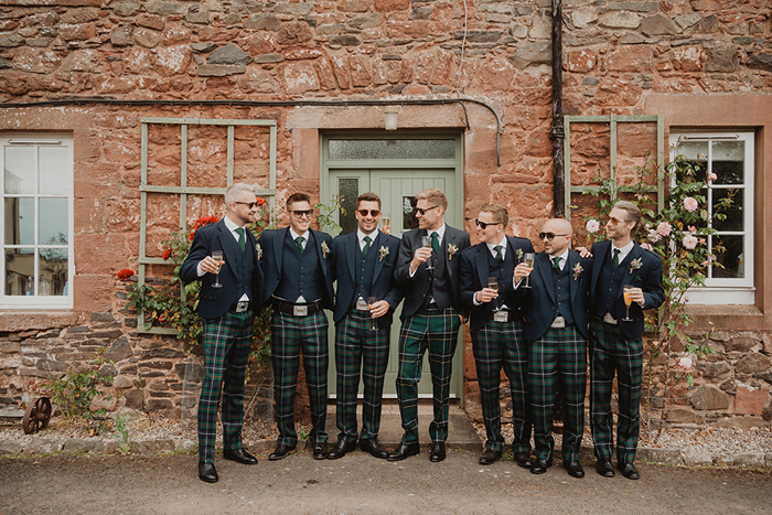 People Wearing Tartan Trousers Standing Against A Red Stone Building