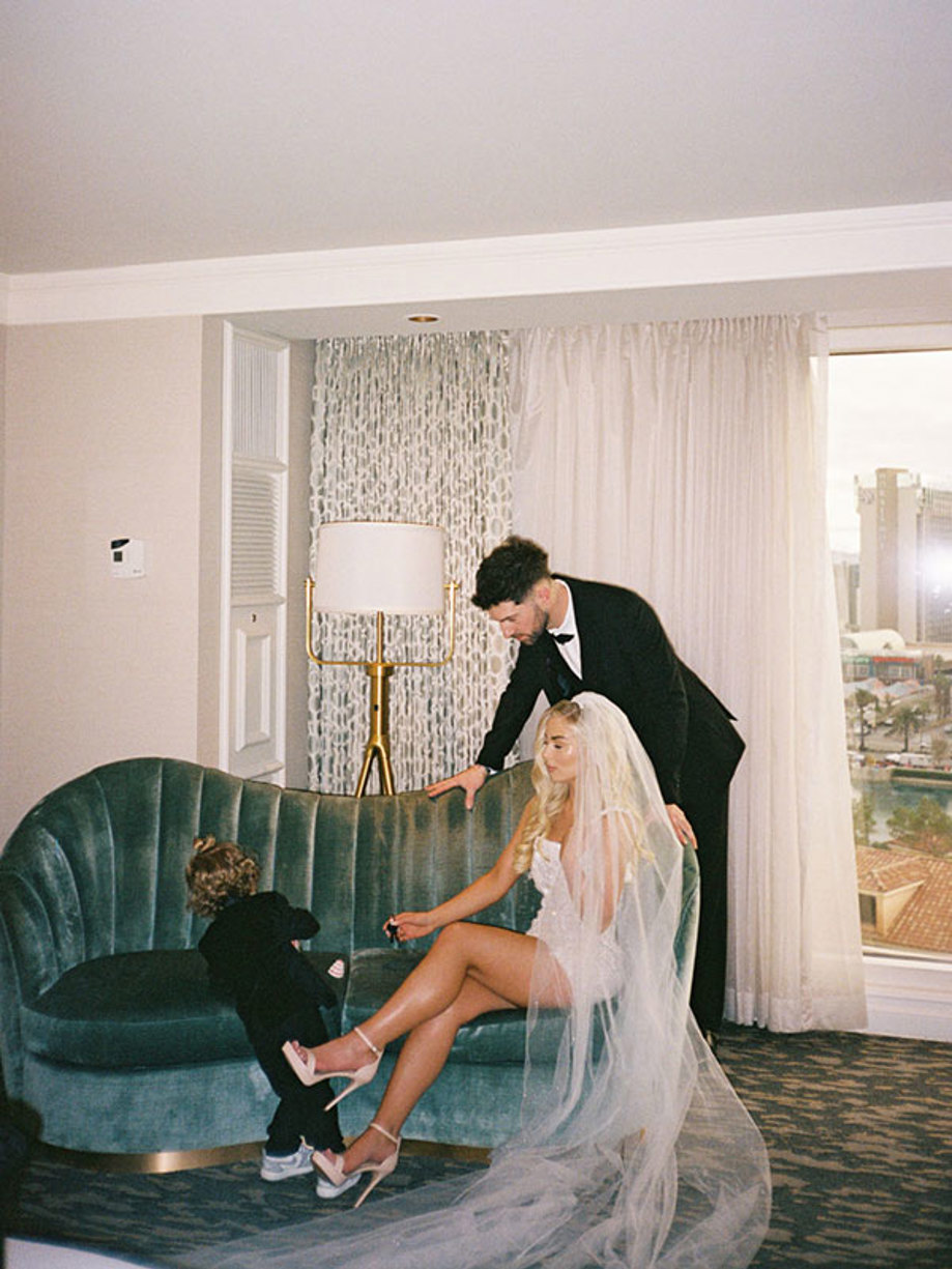 bride, groom and little boy gather around a plush velvet blue-green sofa, all dressed in their wedding day attire 