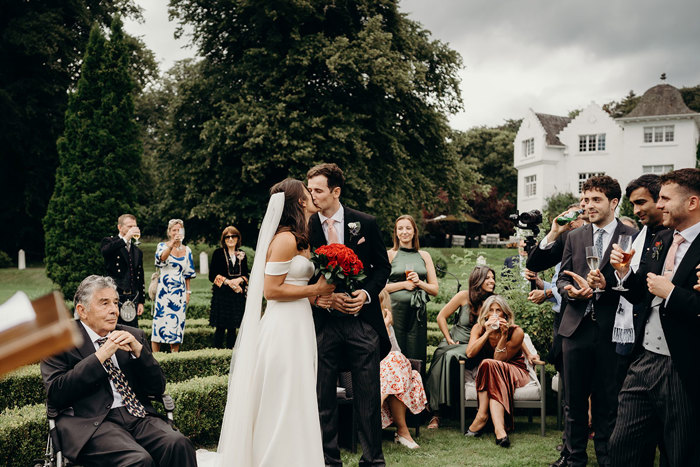 a bride and groom kissing in the garden at Achnagairn Castle as people watch on