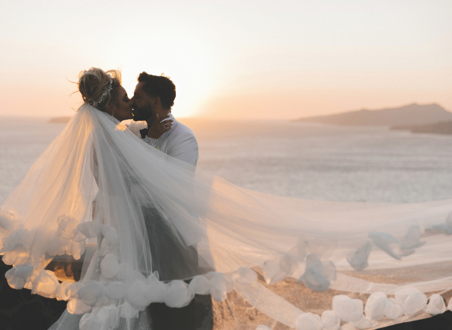 bride and groom kissing with veil flying at sunset