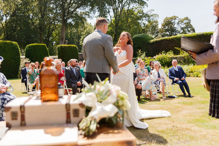 A bride and groom holding hands and smiling during an outdoor ceremony 