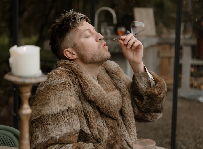 a person wearing a brown fur style jacket blowing bubbles