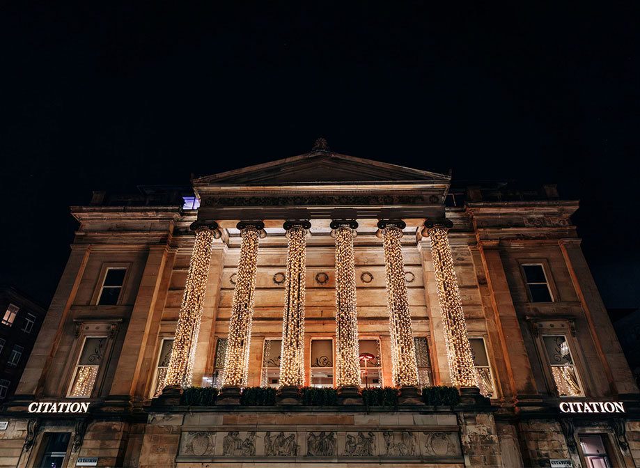 Looking up at the front of a building with six large columns covered in fairylights