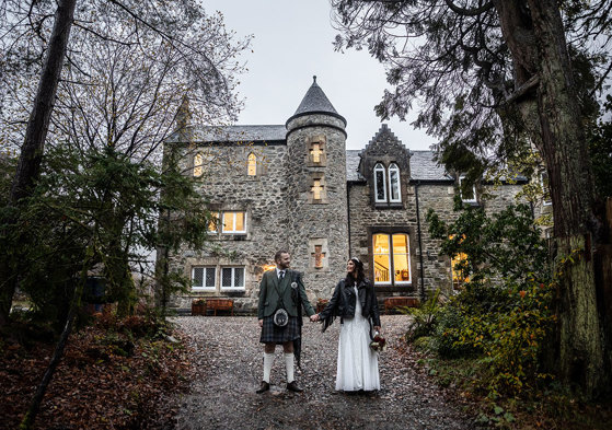 a Scottish wedding day couple holding hands outside a small castle-like building