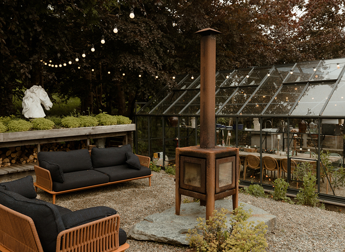 a greenhouse at Kilmartin Castle with black window frames and table set for dinner within. There is a rusty looking firepit and garden seating area beside the greenhouse