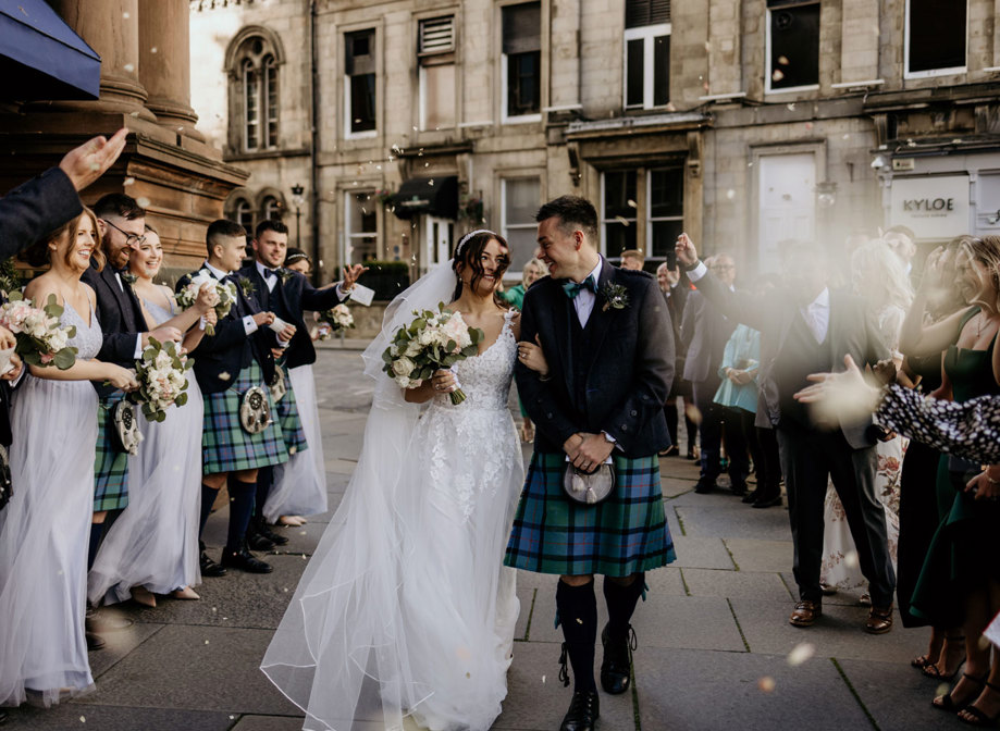 Bride and groom smile as flower petals thrown by friends and family fall around them