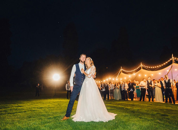 The newly-wed couple stand ahead of their guests, as they all tilt their heads up to watch the fireworks in the night sky