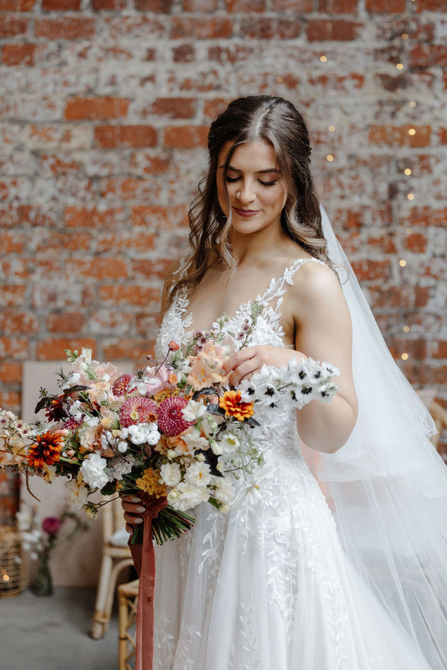 bride with strappy floral applique wedding dress and long low worn veil and holding a wildflower ribbon tied bouquet