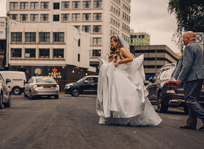 bride with large white dress crossing city centre road with man following behind