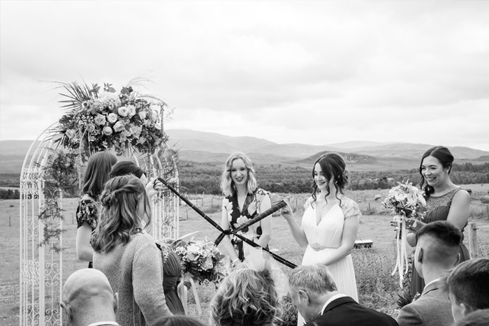 A Black And White Image Of Two Brides Performing A Handfasting At An Outdoors Wedding Ceremony In The Highlands