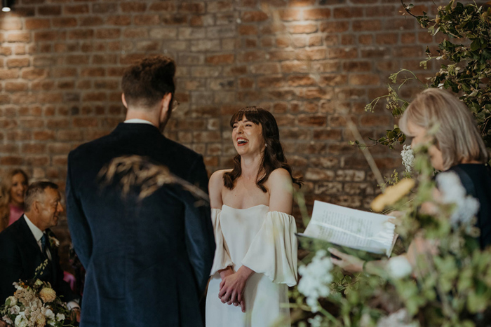 Bride and groom facing each other and bride laughing during ceremony